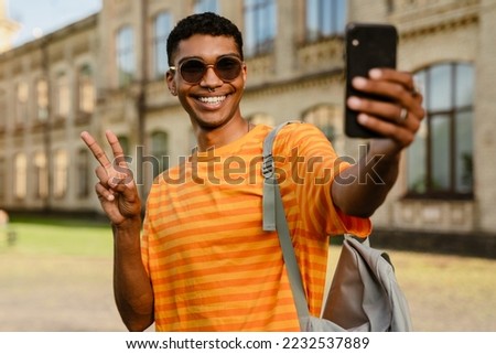 Young black brunette man wearing sunglasses walking outdoors with cellphone