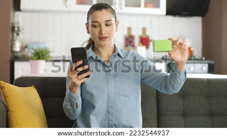 Woman holding smartphone and green box on her sofa, showing a product, smiling and presenting an imaginary object. Creative 3d artists can replace the green box with any product they want.