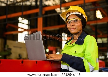 Portrait of female mechanical engineer worker in yellow hard hat and safety uniform using laptop standing at manufacturing area of industrial factory Royalty-Free Stock Photo #2232546113
