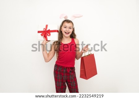 girl holding a gift box and a red package on a gray background, a banner. Beautiful girl with bunny ears ss a package and a gift in her hands.The concept of gifts and sales for christmas. 