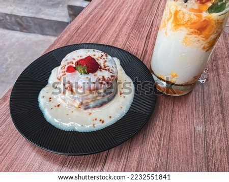 close up photo of pan cake with strawberry topping on top with a mango milkshake drink, suitable for serving as a relaxing menu with family or for inspiration or your digital element needs