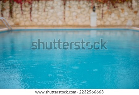 Outdoor swimming pool in rainy weather, rainy season, abstract blurry summer background for resort hotel pool party, screensaver idea