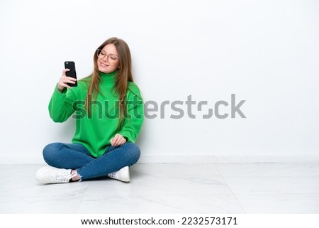Young caucasian woman sitting on the floor isolated on white background making a selfie