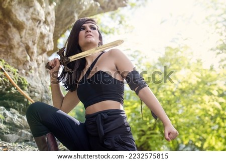 Beautiful warrior girl with sword in hand hidden among rocks - warrior woman concept