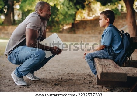 School teacher motivating a young primary school kid outside class. Child mentor talking to a troubled school boy. Support and encouragement for a student in elementary school. Royalty-Free Stock Photo #2232577383