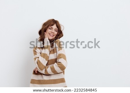 a sweet, thoughtful, pleasant woman stands on a light background in a striped sweater and holds her hand near her face. Horizontal heart rate photo with empty space