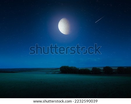 Big bright moon in the night sky over the fields. Night landscape with full moon and falling star.