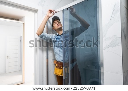 Handyman installing glass cabinet in bathroom. Royalty-Free Stock Photo #2232590971
