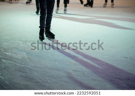 Ice skaters on ice rink, skates close up. People having fun and skating in town square in evening.Legs with ice skaters cropped view. Atmospheric Winter holidays in Europe. Happy Holidays!