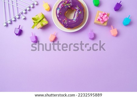 Jewish holiday Hanukkah concept with donuts, menorah, spinning tops and gift box on purple background. Top view, flat lay