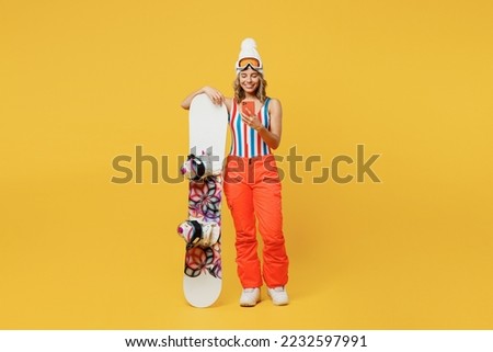 Snowboarder fun woman wear orange suit goggles mask hat ski costume swimsuit spend extreme weekend hold use mobile cell phone isolated on plain yellow background. Winter sport hobby trip relax concept