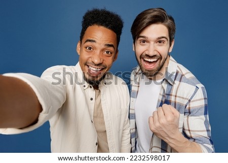 Close up young two friends fun men wear white casual shirts together do selfie shot pov on mobile cell phone do winner gesture isolated plain dark royal navy blue background. People lifestyle concept