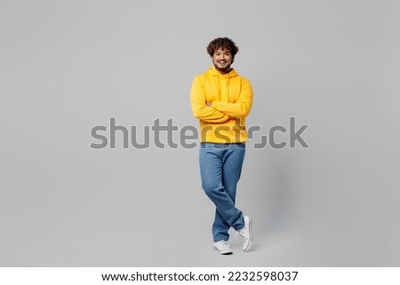 Full body young smiling happy student calm Indian man 20s with mustache and curly hair, he wear casual yellow hoody hold hands crossed folded isolated on plain grey color background studio postrait Royalty-Free Stock Photo #2232598037