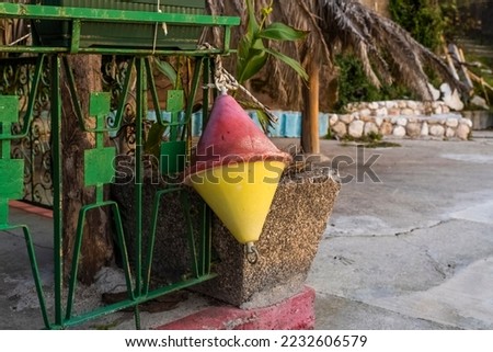 Close-up of an old two-color red and yellow marine buoy hanging near coastal fishing boats. Tools for fishing.