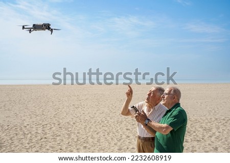 elderly couple have fun with a flying drone flying in a beach with blue sky