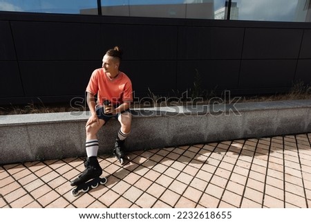 Positive man in earphone and roller blades holding paper cup outdoors at daytime