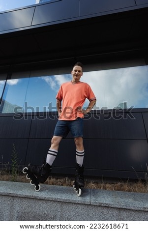Wide angle view of smiling man in roller blades standing on parapet outdoors
