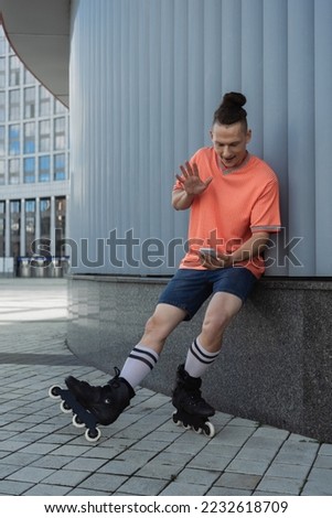 Roller skater in casual clothes having video call on smartphone near building outdoors