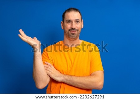 Handsome latino man with beard over isolated blue background holding imaginary copyspace on palm.