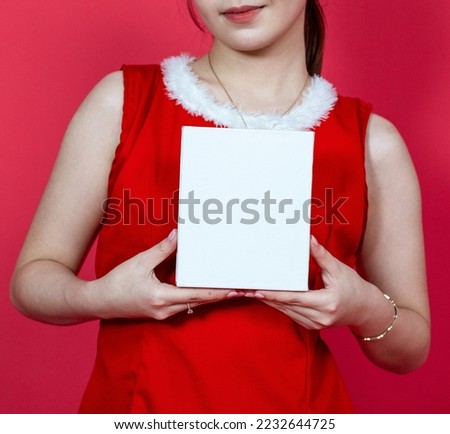 White blank small gift box mockup image featuring a young asian woman presenting the box with a christmas theme on a red background