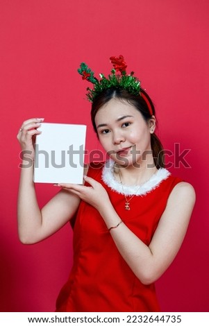 White blank small gift box mockup image featuring a young asian woman presenting the box with a christmas theme on a red background
