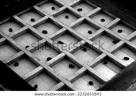 Close-up of an ancient wooden game with squares and small black pips. Black and white photo.
