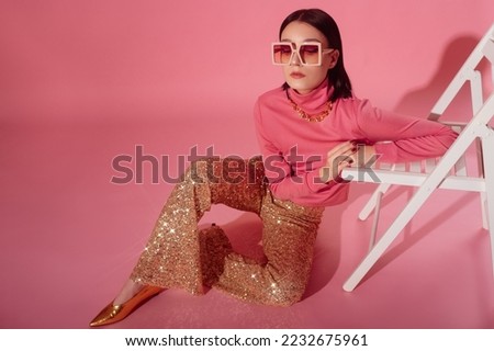 Fashionable confident woman wearing trendy 70s style outfit with big sunglasses, pink turtleneck top, sequined flare trousers, golden  shoes. Full-length studio portrait. Copy, empty space for text Royalty-Free Stock Photo #2232675961
