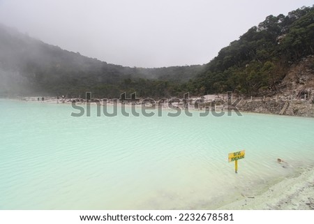 The sulfur lake at Ciwidey in West Java, Indonesia known as Kawah Putih or white crater. 
The yellow sign in the water with the Indonesian words "batas pengunjung" translates as visitors limit". 