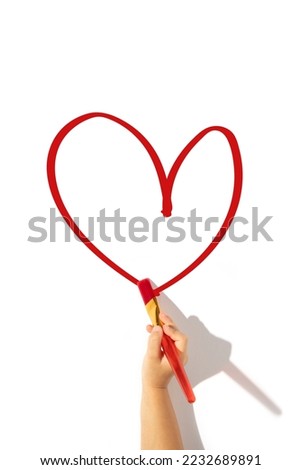 Сhild's hand draws a red heart with a brush on a white background. Top view, flat lay.