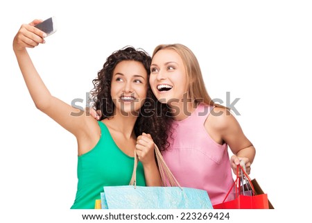 Beautiful smiling young women with shopping bags in hands making photo on telephone, isolated on white