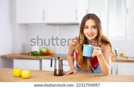 Portrait of relaxed young woman drinking coffee or tea in morning at kitchen