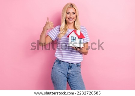Portrait of attractive positive person hold little house demonstrate thumb up isolated on pink color background