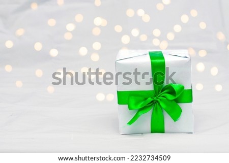 Decorative white gift box with a large green bow against a background bokeh of lights