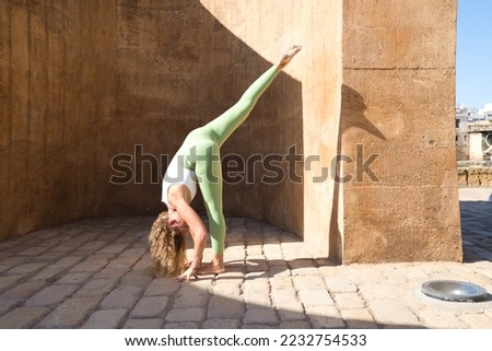 Beautiful middle-aged woman doing yoga in the street. The woman is doing relaxation and tranquility postures. Woman is wearing green leggings and white top. Health and sport concept