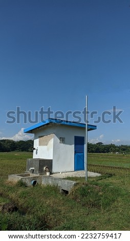photo of a watering hut in the middle of a lush paddy field, with a clear blue sky