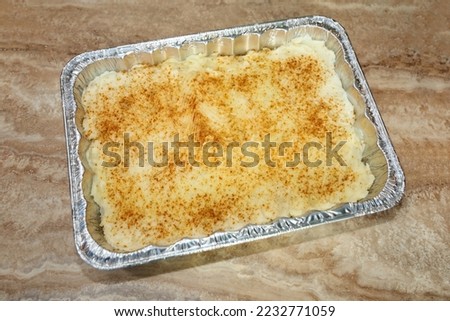 Mashed potatoes on a disposable foil baking dish sprinkled with paprika for color ready to be baked.