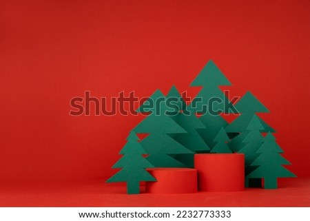Christmas art two cylinder podiums and red stage for presentation gifts, cosmetic products, goods, green paper spruces in cartoon style, copy space. New year template for advertising, design.