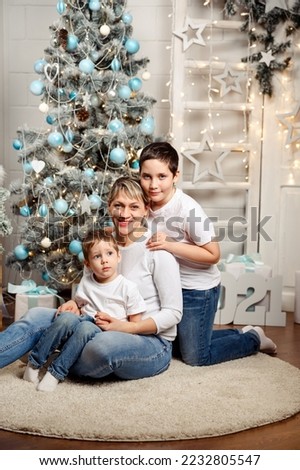 Mom and kids decorate the Christmas tree indoors. Portrait of happy family. Portrait loving family close up. Parent and two little children having fun and playing together near Christmas tree.