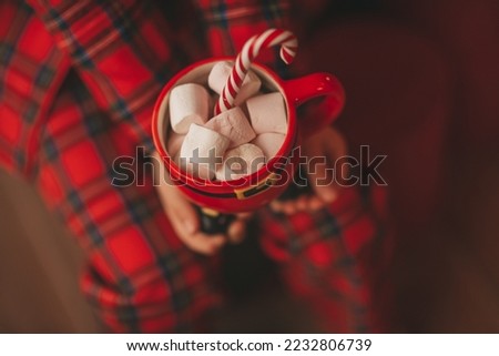 Happy japan little girl dreamer waiting miracle Santa enjoy sweets near noel tree. Asian kid in red plaid outfit celebrating new year hold Xmas cup with marshmallows at bokeh lights eve 25 december