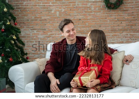 Man wearing santa hat with daughter sitting on couch at home,Celebration,Holidays and christmas concept.