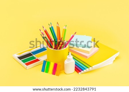A set of stationery for school and office in the assortment. Notebooks, plasticine, pencils, scissors, eraser and glue on a bright yellow background. Side view.