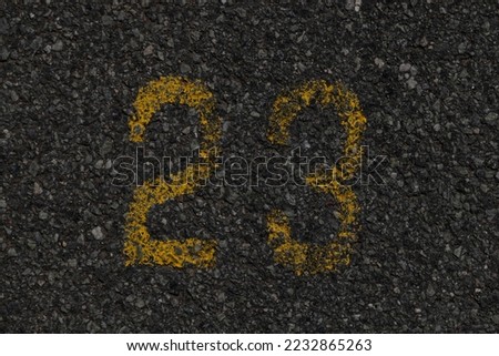In ancient times, the numbers twenty-three were written in yellow letters on dark gray asphalt. Fine pebbles, gloomy, dark picture.