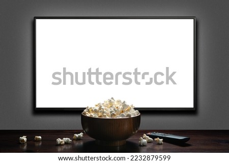 Television on a gray wall with remote control and popcorn bowl on the table. TV 4K flat screen lcd or oled, White blank HD monitor mockup. Modern video panel black flatscreen. Royalty-Free Stock Photo #2232879599