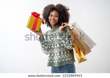 Portrait of young attractive african american woman with curly hair holding shopping bags and gift box in studio on white background.