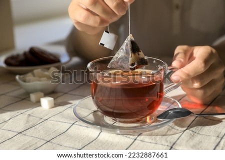Woman taking tea bag out of cup at table indoors, closeup Royalty-Free Stock Photo #2232887661