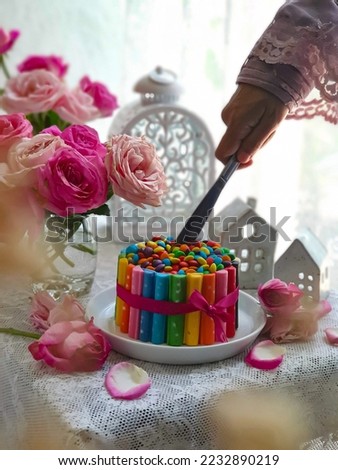 Selective focus of colorful chocolate cake. a bouquet of roses with light and airy shades on a white background. Eye level angle. Hand in frame 