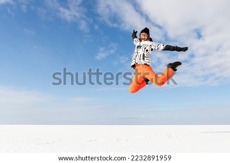 Young adult beautiful sporty happy attractive caucasian smiling hiker woman enjoy jumping high frozen lake surface panorama horizon background. Winter travel freedom outdoors adventure trip concept