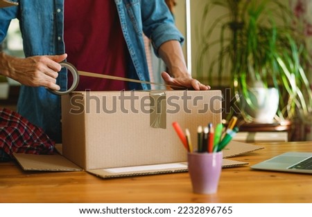 Man sealing parcel with duct tape.  Royalty-Free Stock Photo #2232896765