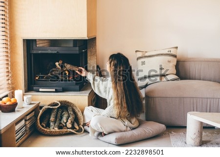 Woman putting firewood in the fireplace and lights it. Cozy evening at home. Royalty-Free Stock Photo #2232898501
