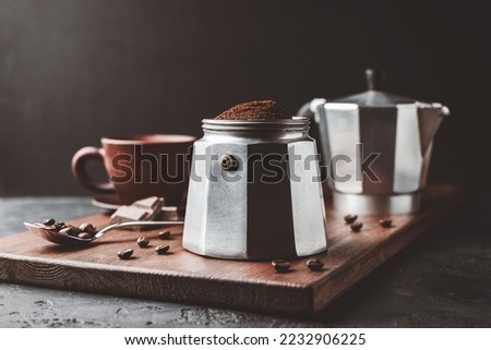 Moka coffee pot filled with brown ground coffee on dark wooden board, prepare to brewing Italian espresso.